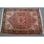 A large rug with geometric repeating motifs on a red ground within three borders,