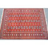 A Caucasian style rug with three rows of thirteen medallions on a red ground