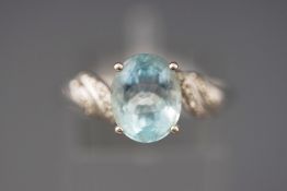 A white metal dress ring. Set with an oval blue topaz and single cut diamond shoulders.
