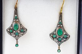 A yellow and white metal pair of drop earrings set with emeralds and single cut diamonds.