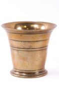 A brass mortar of traditional bell form with turned band decoration,