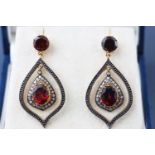 A yellow and white metal pair of drop earrings. Each set with garnets and single cut diamonds.
