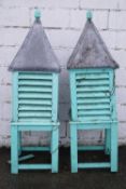 A pair of painted bee houses with acorn finials above a lead roof, on square stands,