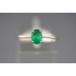 A white metal single stone ring set with an oval faceted cut emerald.