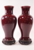 A pair of Sang de Boeuf baluster vases on carved wooden stands,