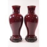 A pair of Sang de Boeuf baluster vases on carved wooden stands,