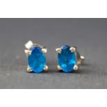 A white metal pair of single stone studs, each set with an oval faceted cut blue Apatite.