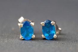 A white metal pair of single stone studs, each set with an oval faceted cut blue Apatite.