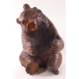 A carved Black forest style bear in seated position with paws out stretched,