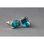 A white metal pair of single stone stud earrings each set with an oval faceted cut blue topaz.