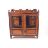 An oak two glazed door smoker's cabinet, opening to reveal two pipe racks and four drawers,