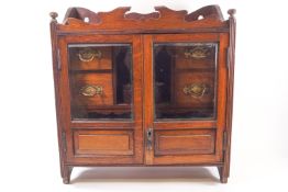 An oak two glazed door smoker's cabinet, opening to reveal two pipe racks and four drawers,