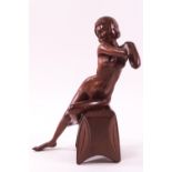 A carved mahogany figure of a seated female nude with crossed hands and legs,