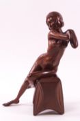 A carved mahogany figure of a seated female nude with crossed hands and legs,