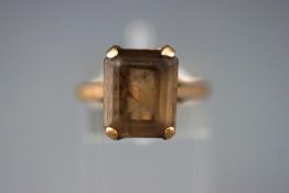 A yellow metal single stone ring set with a rectangular faceted cut smokey quartz.