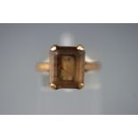 A yellow metal single stone ring set with a rectangular faceted cut smokey quartz.