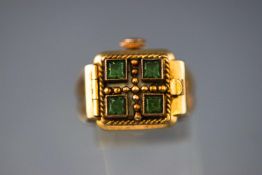 A yellow metal ring having a hinged green stone set fancy top to reveal a small square watch face.