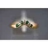 A yellow metal wishbone ring set with emeralds and single cut diamonds.