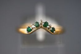 A yellow metal wishbone ring set with emeralds and single cut diamonds.