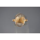A yellow metal single stone ring set with an oval cabochon cut rutilated quartz