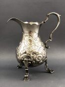 A silver cream jug with cut card edge and scroll handle over a belied body repousse