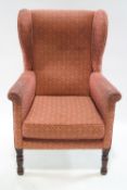 A 19th century style wing armchair upholstered in red with one loose cushion, on turned legs,