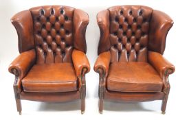 A pair of wing back arm chairs upholstered in deep buttoned brown leather