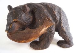 A carved black forest style figure of a bear holding a salmon in his mouth,