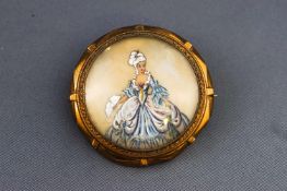A yellow metal circular painted portrait brooch. Pin and hook fittings. No hallmark.