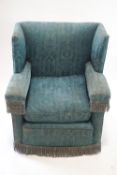 A blue upholstered wing armchair with fringes to the arms and base, 92cm high, 83cm wide,
