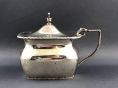 A silver rectangular mustard pot with domed lid topped with an urn over a bellied body