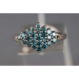 A white metal cluster ring set with round faceted cut treated blue diamonds (one is missing).