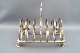 A silver six slice toast rack with central trefoil strap handle and dividers on ribbed base and