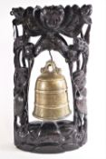 A brass temple bell, of traditional form, with naturalistic handle set on a carved hardwood stand,