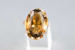 A yellow metal single stone ring set with a large oval faceted cut smokey quartz.