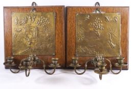 A pair of oak wall candlelight sconces each with embossed brass panel, with a chinoiserie scene,