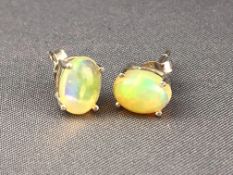 A white metal pair of single stone stud earrings each set with an oval cabochon opal.