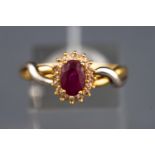 A yellow and white metal cluster ring set with an oval faceted cut ruby