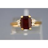 A yellow metal dress ring set with a rectangular cut garnet and four round brilliant cut diamonds.