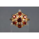 A yellow metal cluster ring set with almandine garnet and illusion set single cut diamonds.