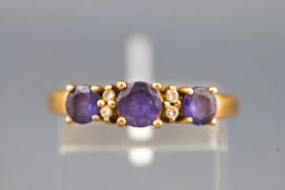 A yellow metal dress ring set with three round faceted cut tanzanite