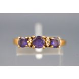 A yellow metal dress ring set with three round faceted cut tanzanite