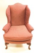 An upholstered wing back armchair on carved mahogany cabriole legs