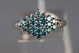 A white metal cluster ring set with round faceted cut treated blue diamonds (one is missing).