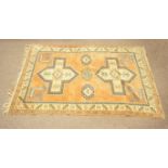A cream ground rug with three hooked lozenges flanked by two cruciform medallions on an orange