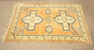 A cream ground rug with three hooked lozenges flanked by two cruciform medallions on an orange