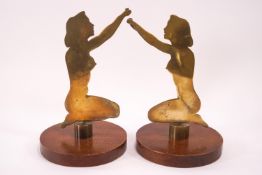 A pair of brass figures of naked kneeling ladies on round oak bases,