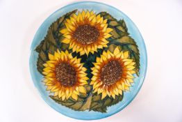 A Moorcroft charger decorated with naturalistic sunflower heads on a turquoise ground,