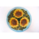 A Moorcroft charger decorated with naturalistic sunflower heads on a turquoise ground,