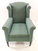 A wing armchair with green upholstery on ebonised square tapering legs amd cast metal casters